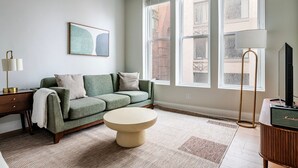 Een woonkamer met een groene bank, een ronde salontafel, een lamp en een televisie op een houten dressoir.