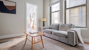 A living room with a grey sofa, a wooden coffee table, and a painting on the wall. - Blueground | Downtown Crossing, view, nr Boston Common (Boston)