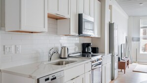 Una cocina moderna con armarios blancos, un lavamanos de acero inoxidable, una cafetera y un horno empotrado.