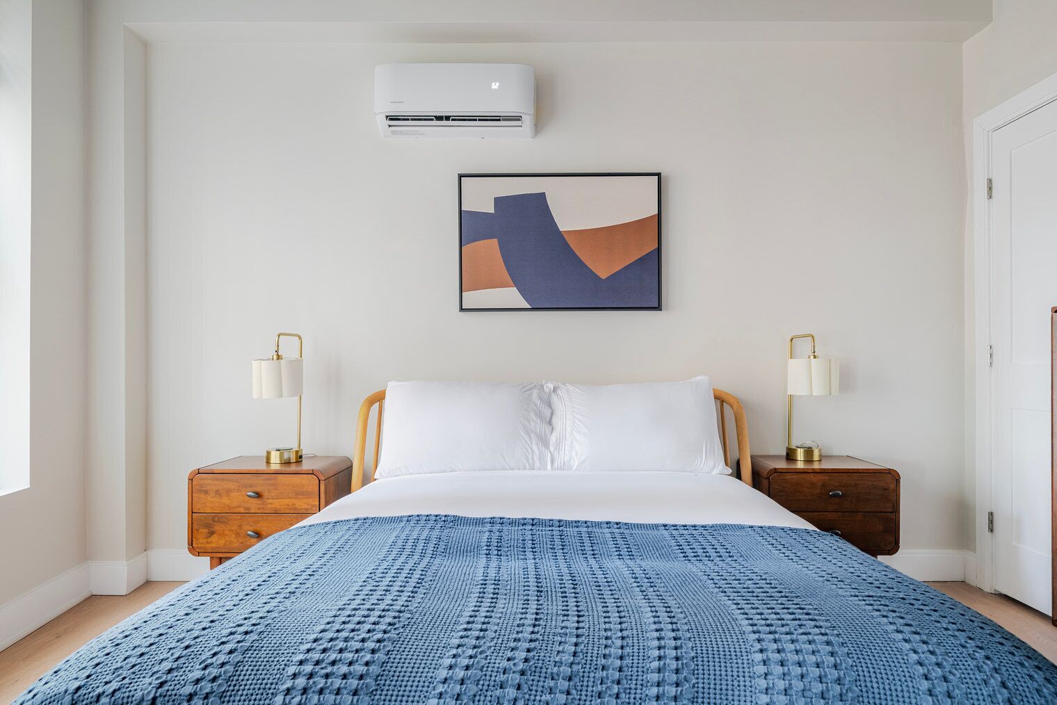 Een slaapkamer met een bed, twee nachtkastjes, een wandairconditioner en een lijst met een abstract schilderij.