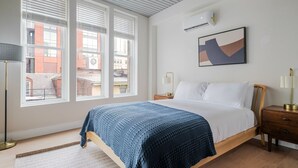 Un dormitorio con cama, mesita de noche, lámpara y ventana con persianas.