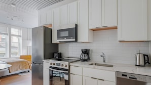 Una cocina moderna con armarios blancos, un refrigerador de acero inoxidable, un microondas, una cafetera y un lavavajillas.