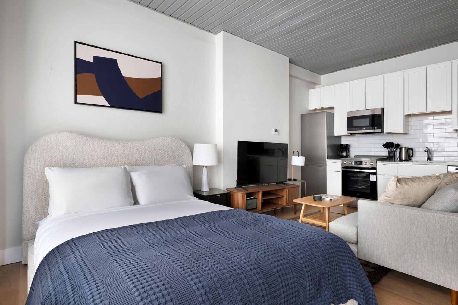 Ein modernes Hotelzimmer mit einem großen Bett, einem Fernseher, einem Schreibtisch, einer Couch und einer Küchenzeile.