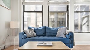 Een moderne woonkamer met een blauwe bank, een houten salontafel en een transparante opbergunit.
