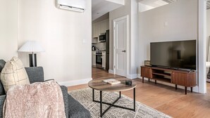 Ein modernes Wohnzimmer mit Sofa, Couchtisch, Fernseher und einer Küche im Hintergrund.