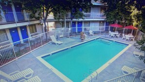 Una piscina con área delimitada, sillas de descanso y un edificio con puertas azules al fondo.