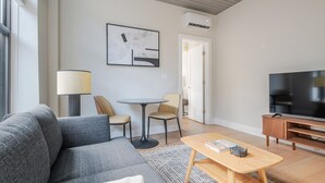 Ein modernes Wohnzimmer mit einem grauen Sofa, einem runden Tisch und einem Flachbildfernseher.