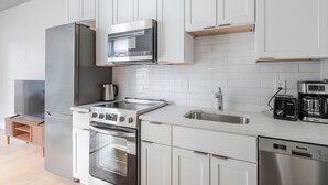 Eine moderne Küche mit weißen Schränken, Edelstahlgeräten, einem eingebauten Backofen, einer Mikrowelle, einer Kaffeemaschine und einem Geschirrspüler.