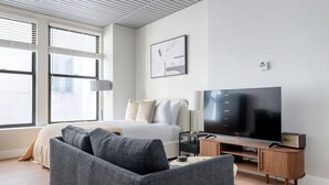A modern hotel room with a bed, a gray sofa, a TV, and a lamp. - Blueground | Downtown Crossing, view, nr Boston Common (Boston)