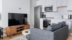 A modern kitchen with white cabinets, a built-in oven, and a microwave. A grey sofa and a TV are in the living area. - Blueground | Downtown Crossing, view, nr Boston Common (Boston)