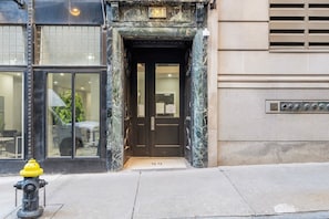 L’entrée d’un immeuble avec une façade en marbre, une porte noire et une borne d’incendie sur le trottoir.