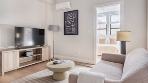 Een moderne woonkamer met een flatscreen televisie, een rond bijzettafeltje, een bank en een lamp.