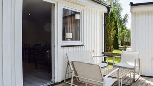 An outdoor seating area with a table and chairs, a window with a curtain, and a view of a garden. - Amazing home in Ystad with WiFi (Ystad)
