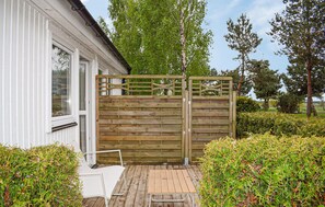 Ein Holztor, ein weißes Gebäude und eine Holzterrasse mit einem Stuhl.