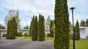 Une rangée de maisons mobiles blanches, chacune dotée d’une porte numérotée, entourée de haies verdoyantes bien entretenues et bordée d’une allée en gravier.