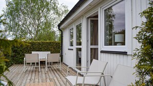 A wooden deck with outdoor furniture, a white building with large windows, and a hedge in the background. - Amazing home in Ystad with WiFi (Ystad)