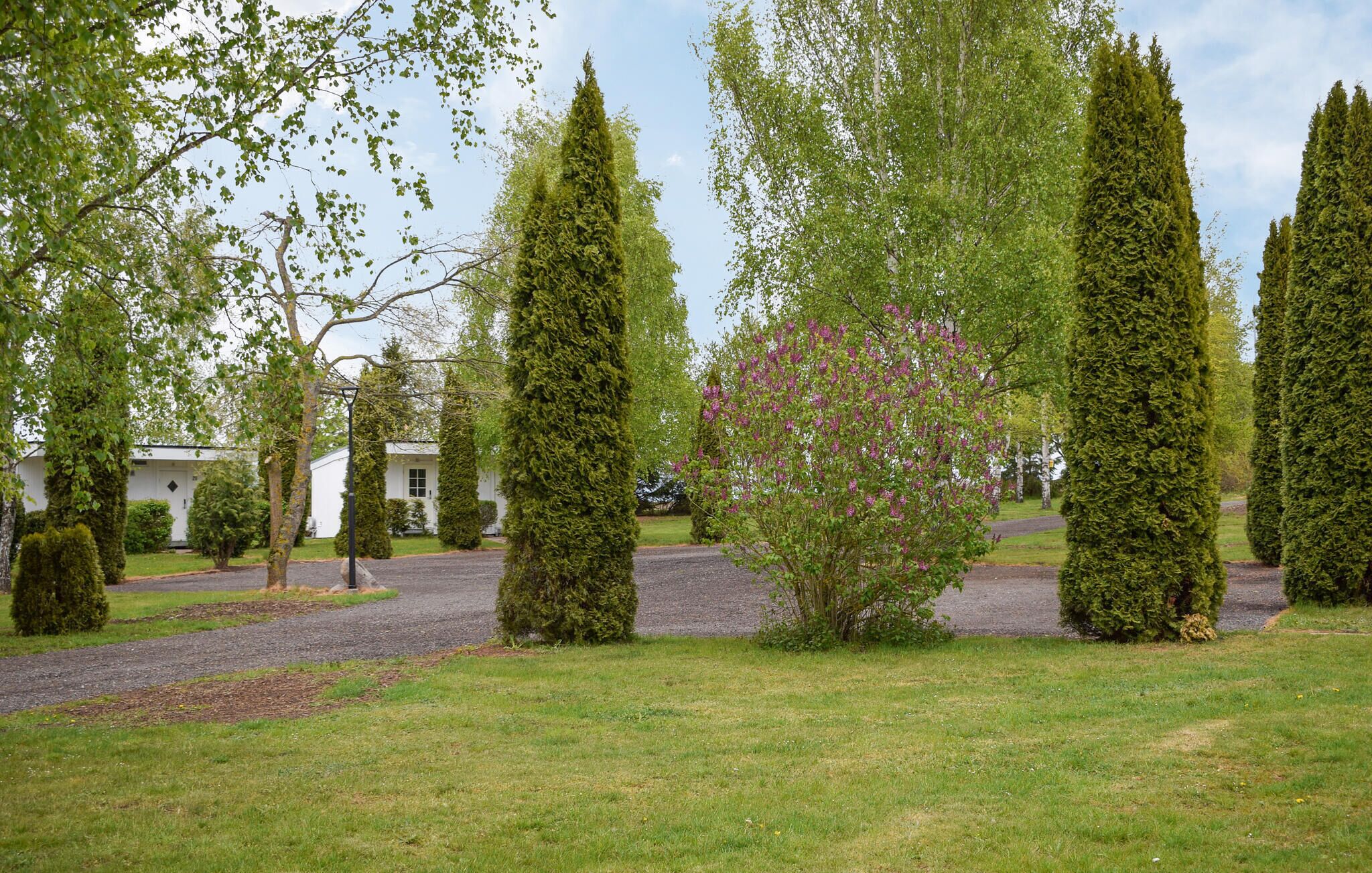 A landscaped garden with neatly trimmed hedges, a gravel path, and a white building in the background.