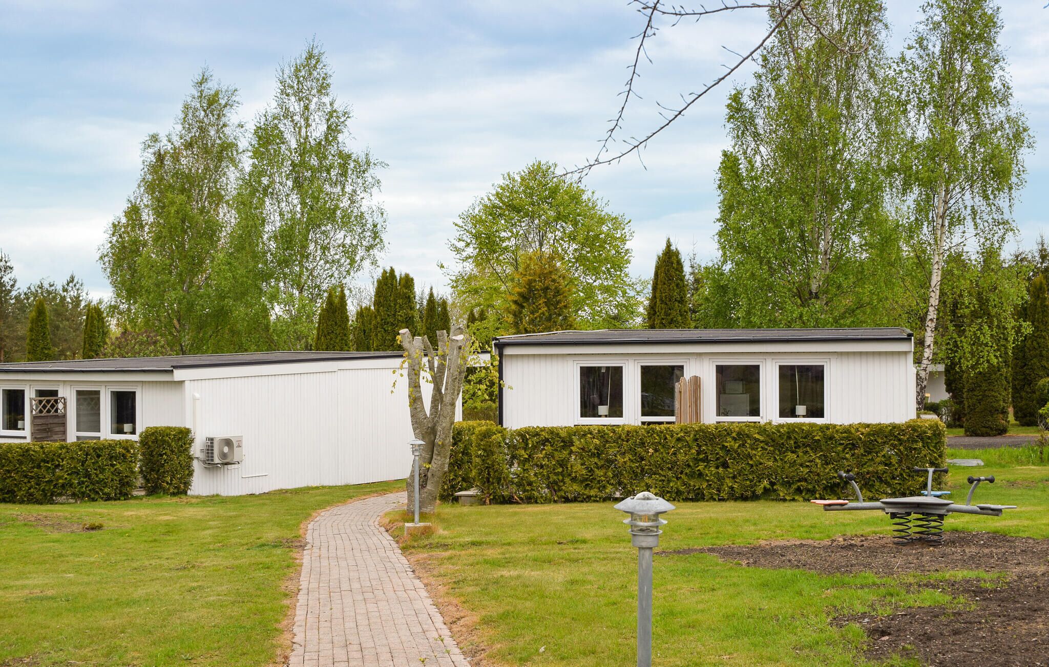 A row of white mobile homes with a paved pathway leading to them, surrounded by greenery and trees.