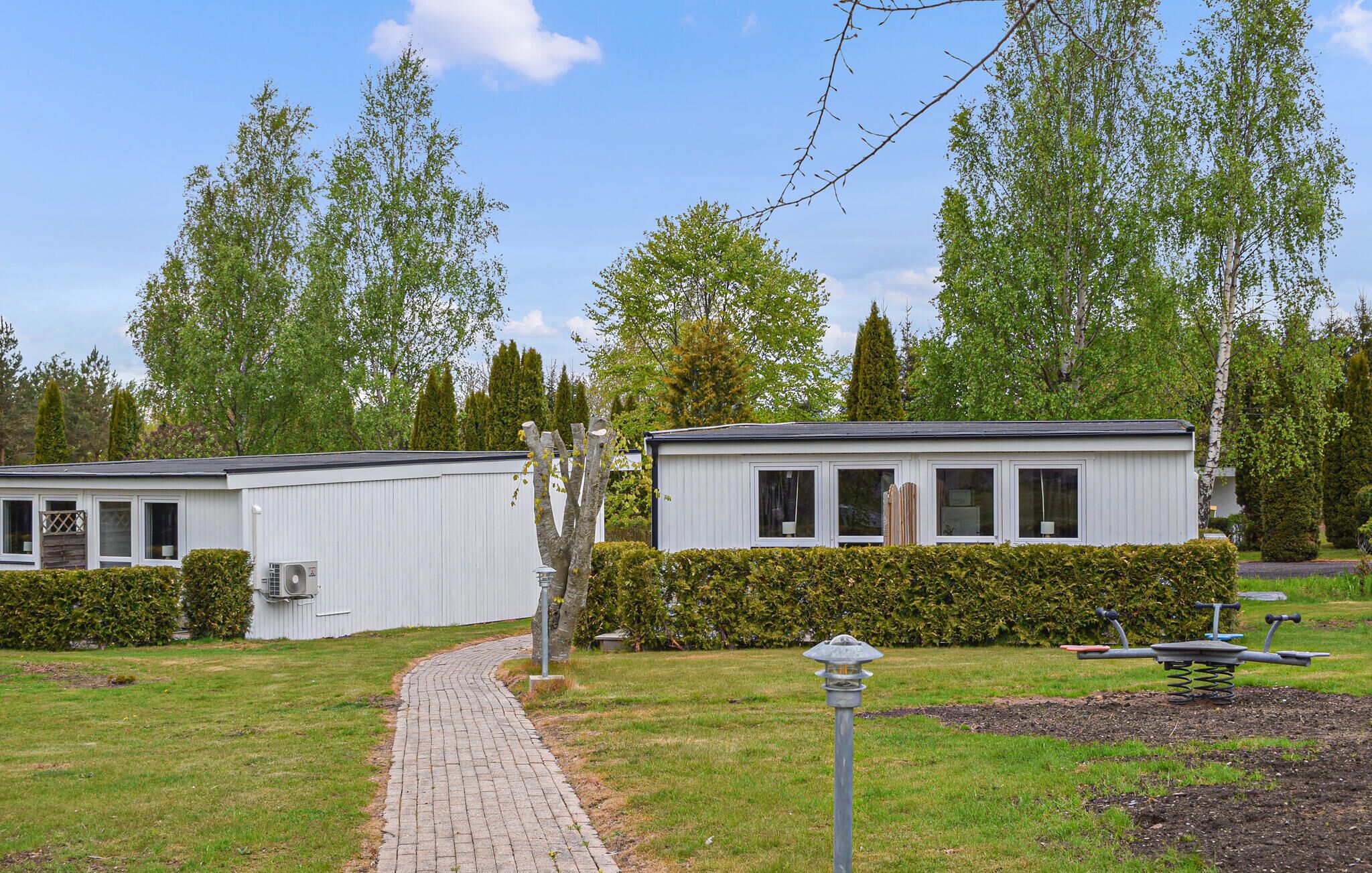 A row of white mobile homes with windows and a paved pathway leading to them.