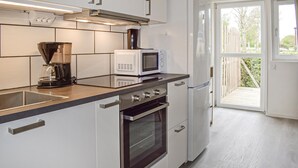 Cozinha moderna com cafeteira, micro-ondas, forno e uma porta de vidro deslizante que dá para uma varanda.