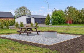 Ein Picknickplatz mit Tisch und Bänken, umgeben von Kies und Gras, mit einem Gebäude im Hintergrund.