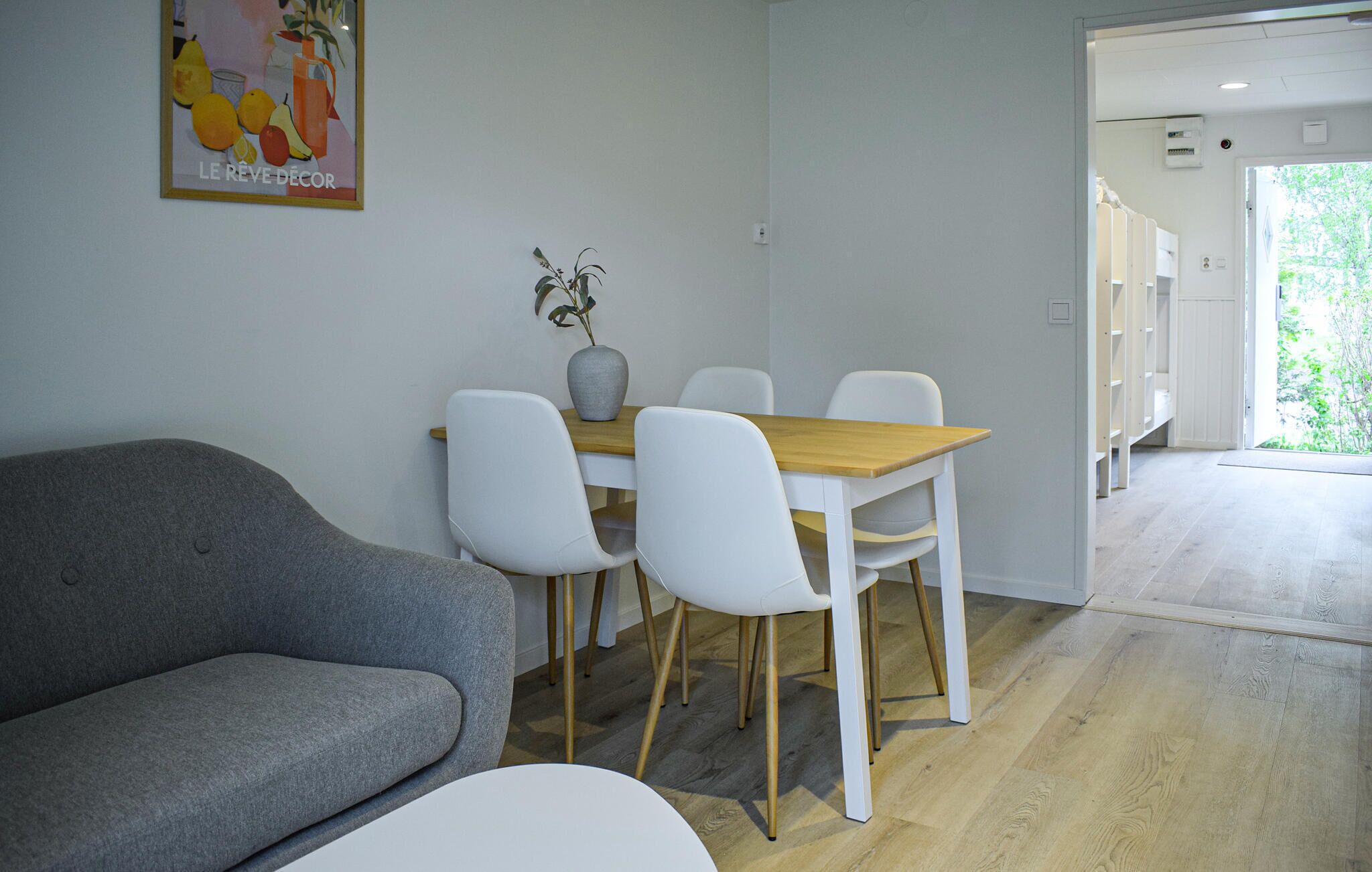 A modern interior with a grey sofa, a wooden dining table with white chairs, and a vase with flowers.