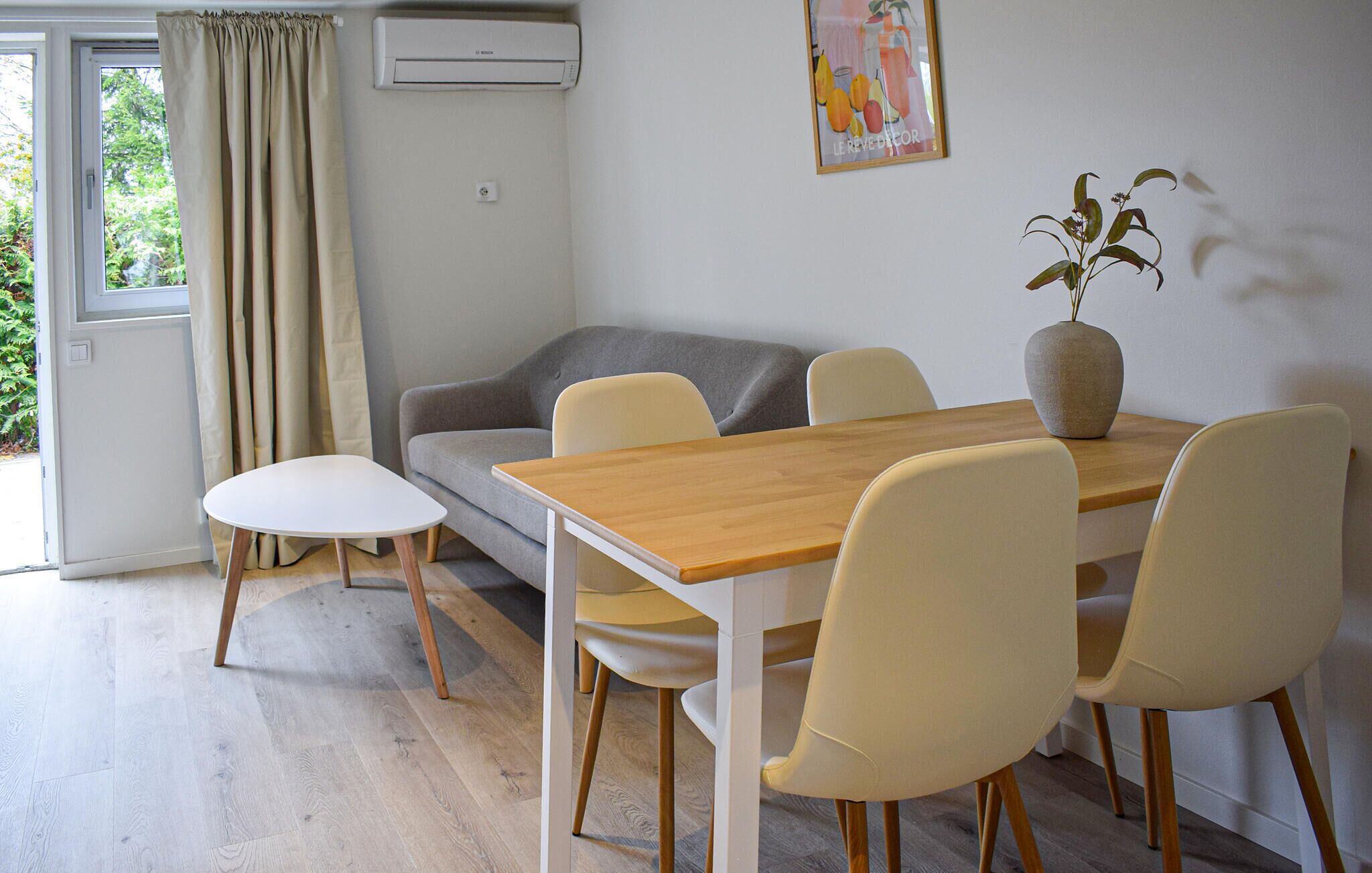 A modern living room with a sofa, a dining table with chairs, a potted plant, and an air conditioning unit.
