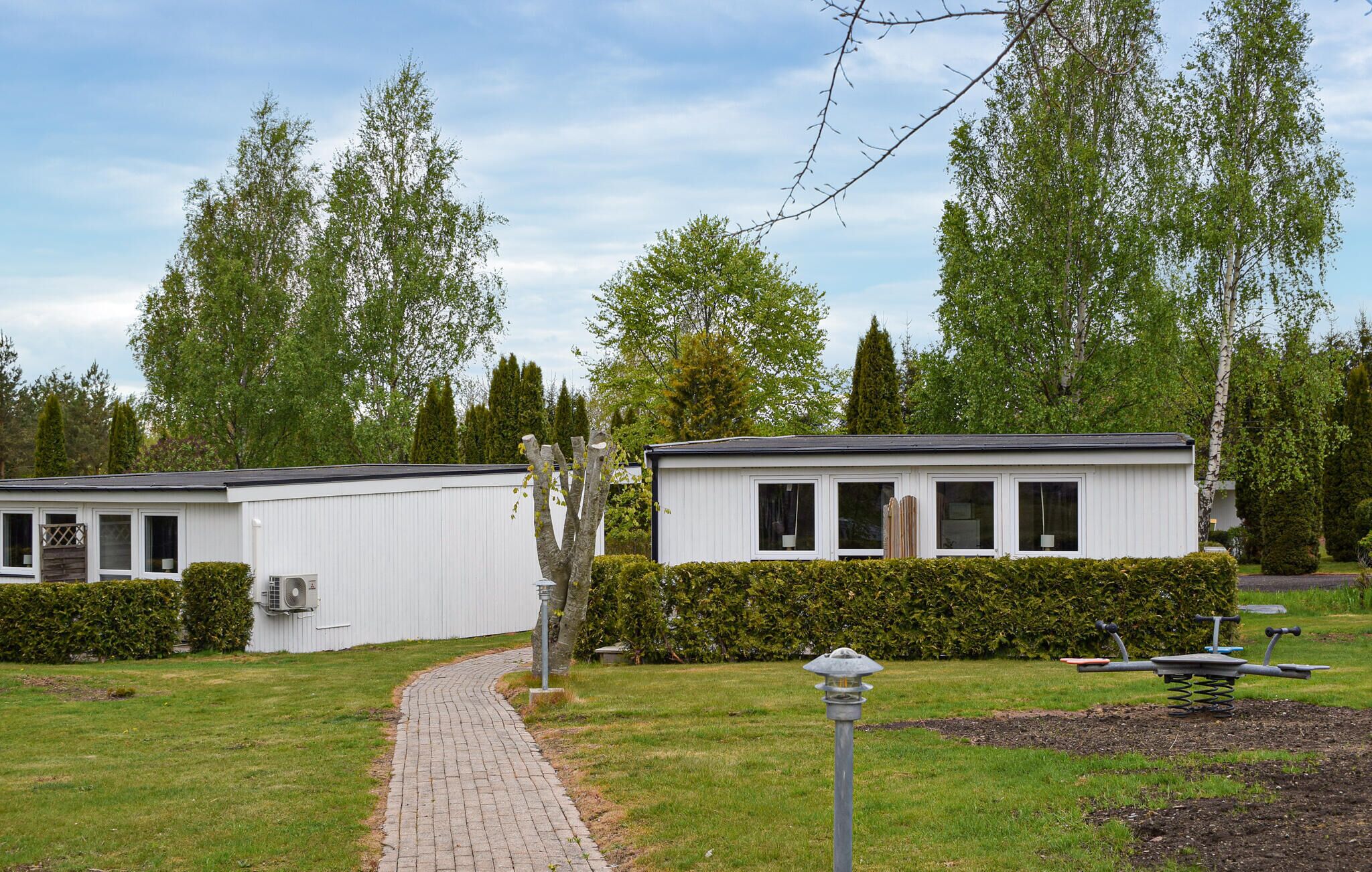 A row of white mobile homes with a paved pathway leading to them, surrounded by greenery and trees.