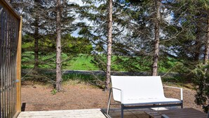 En træterrasse med en hvid stol og et lille bord, omgivet af træer og græs.