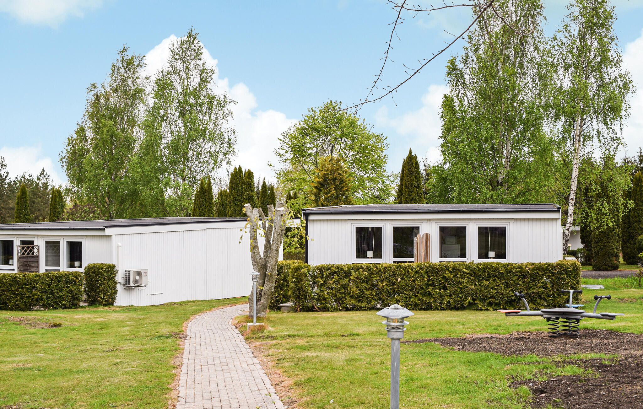 A row of white mobile homes with a paved pathway leading to them, surrounded by greenery and trees.