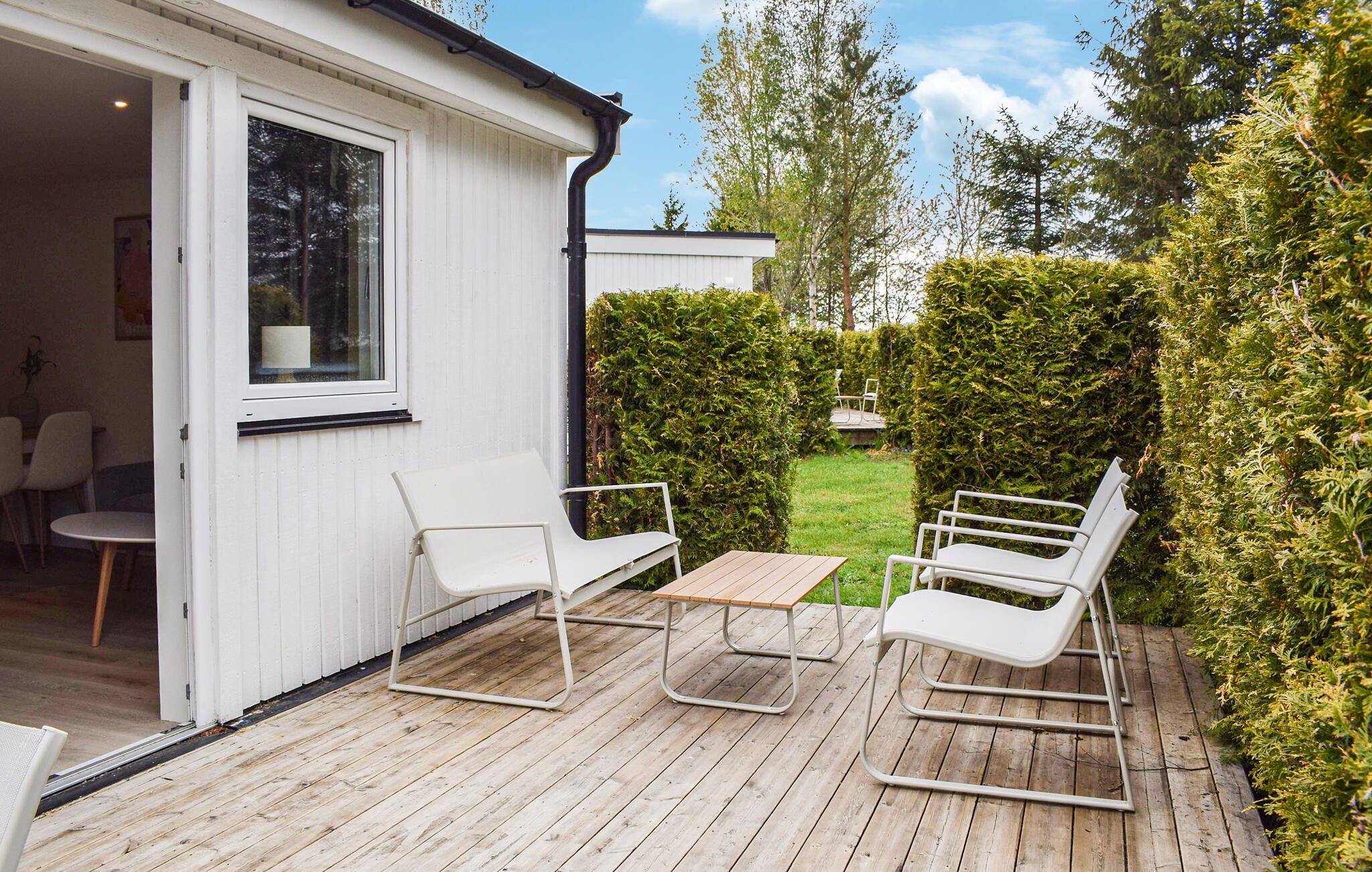 A patio with a table and four chairs, a wooden deck, and a white building with a window.