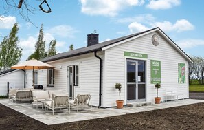 A white building with a reception desk, outdoor seating, and a sign welcoming visitors. - Nice home in Ystad with WiFi (Ystad)