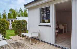 A white mobile home with a patio area, a sliding door leading to an interior dining space, and a view of a garden with trees. - Beautiful home in Ystad with WiFi (Ystad)