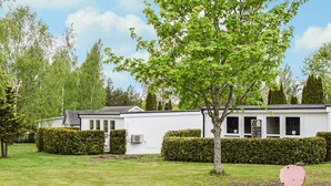 Een witte stacaravan met een kleine tuin, een boom en een roze voorwerp op de voorgrond.