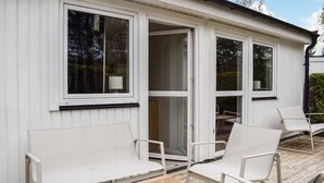 Een wit gebouw met grote ramen en een houten terras met witte stoelen.