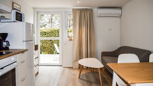 Een compacte keuken met een magnetron, koffiezetapparaat en oven. Een schuifpui geeft toegang tot een balkon met uitzicht op groen.