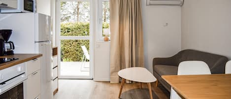 Cocina compacta con microondas, cafetera y horno. Una puerta corrediza de vidrio da a un balcón con vistas a la vegetación.