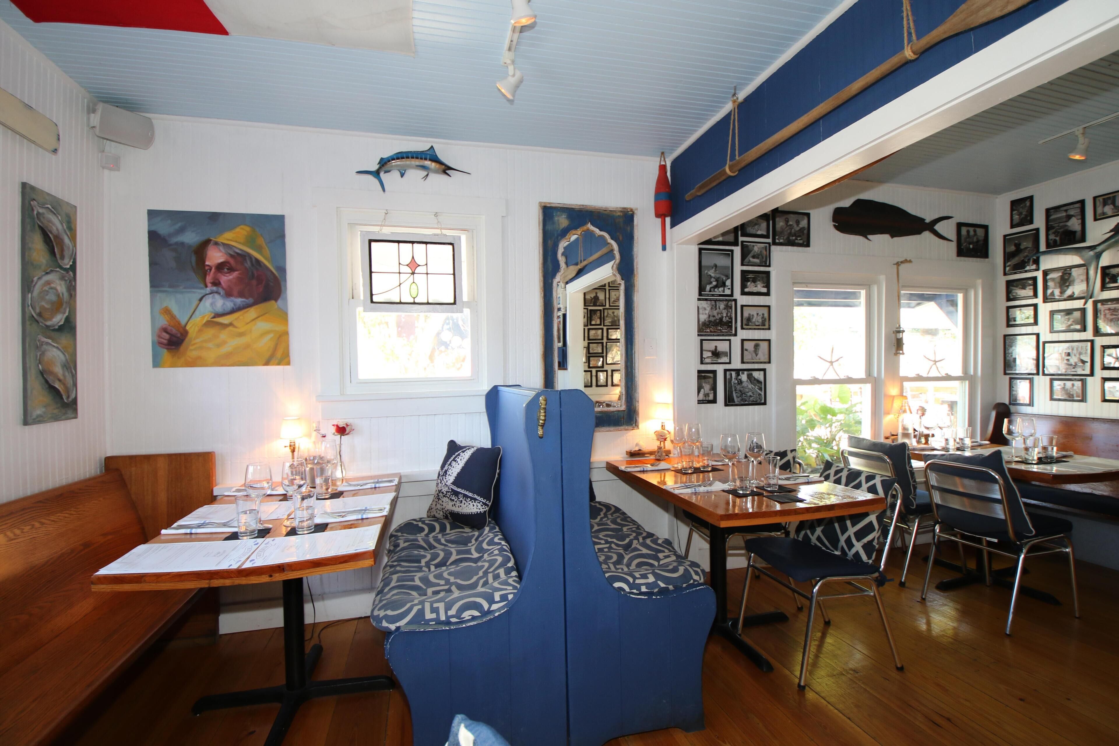 A restaurant with wooden tables and blue cushioned seating, decorated with maritime-themed artwork and photographs.