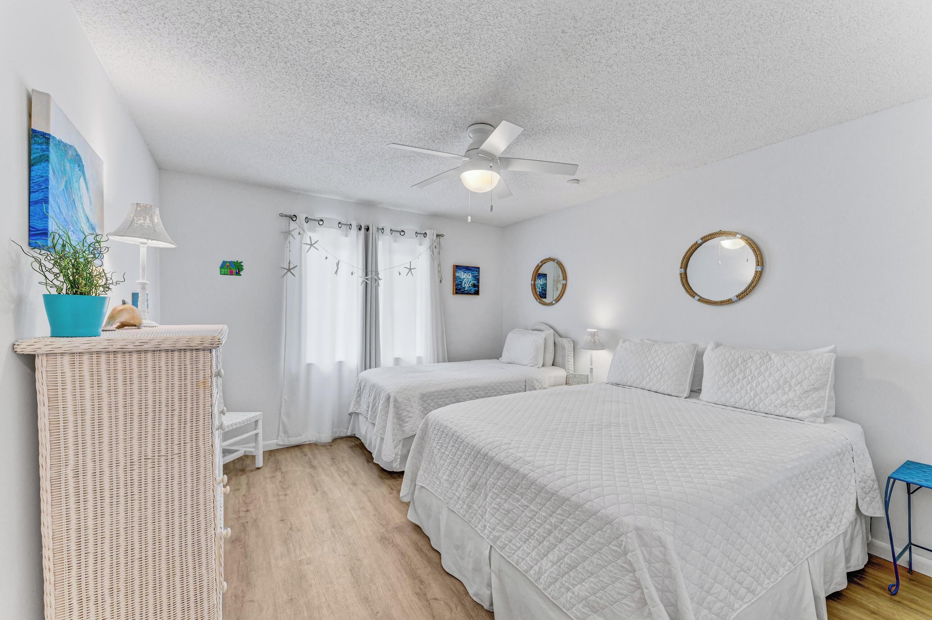 A bedroom with two beds, a ceiling fan, a potted plant, and a small table.