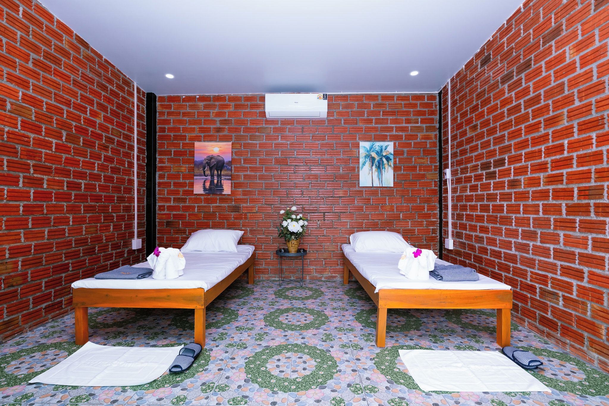 Una habitación con dos camas, una mesita con un florero y un aire acondicionado de pared.