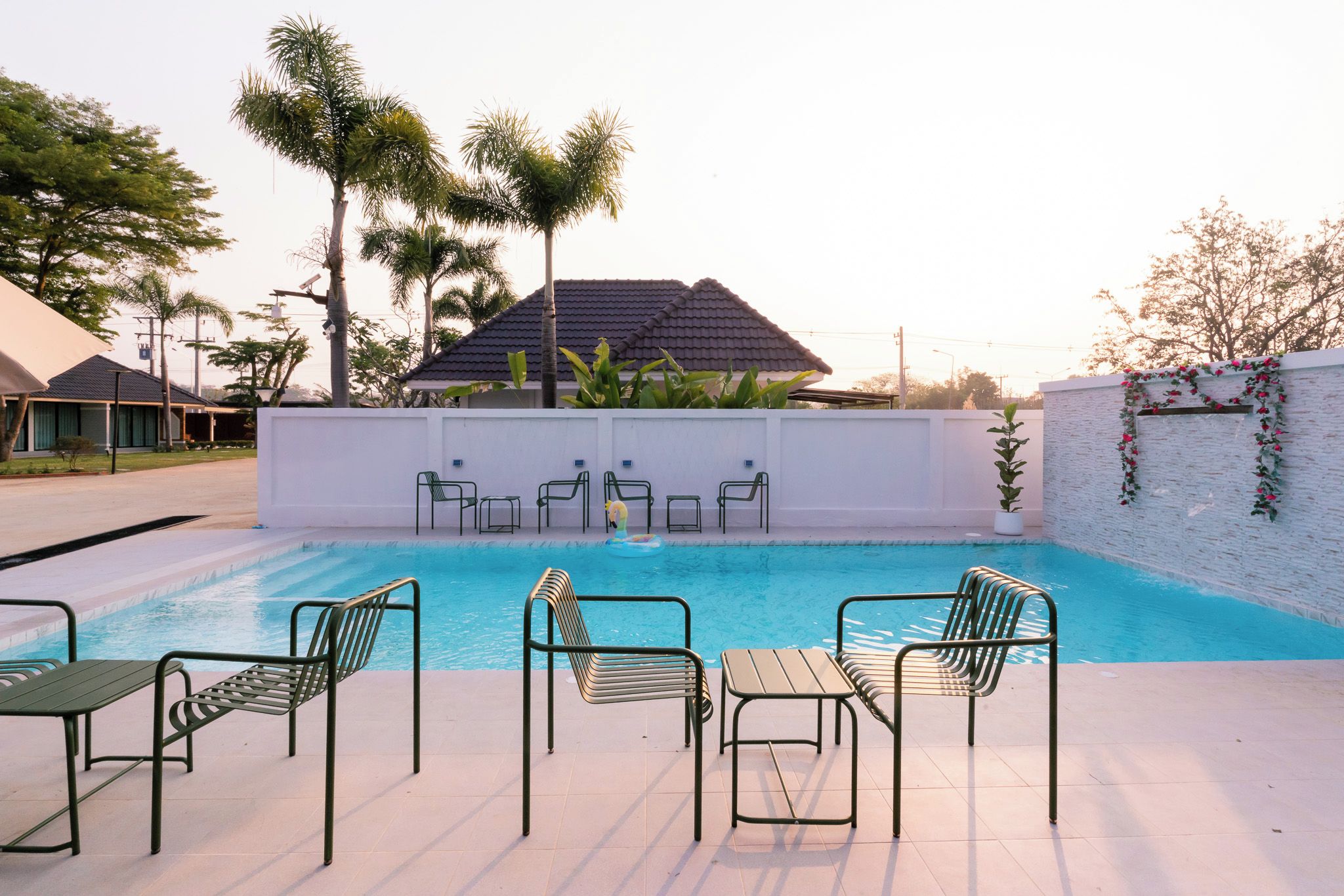 Une piscine avec des chaises longues et un mur blanc percé d’un portail.