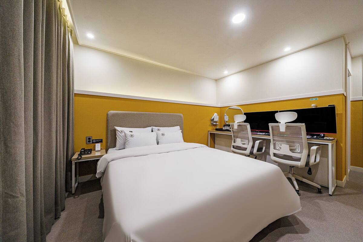 Una habitación de hotel con una cama grande, un escritorio con una computadora y una silla.