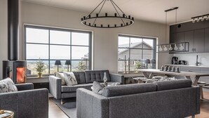 Ein modernes Wohnzimmer mit Kamin, grauen Sofas und großen Fenstern mit Blick ins Freie.