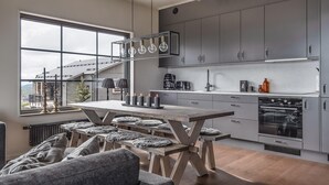Eine moderne Küche mit grauen Schränken, einem Holzespeisetisch mit Bänken und Blick auf ein Gebäude.