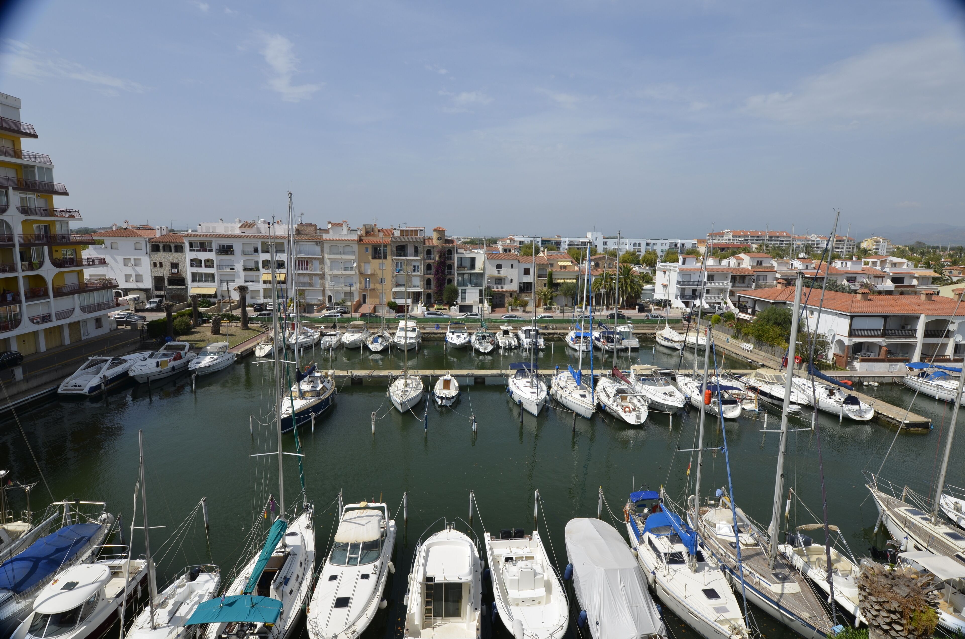 Un puerto deportivo con varias embarcaciones amarradas, rodeado de edificios de varios pisos con balcones.