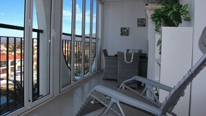 Un balcon donnant sur un paysage urbain, un réfrigérateur blanc et une chaise en osier.