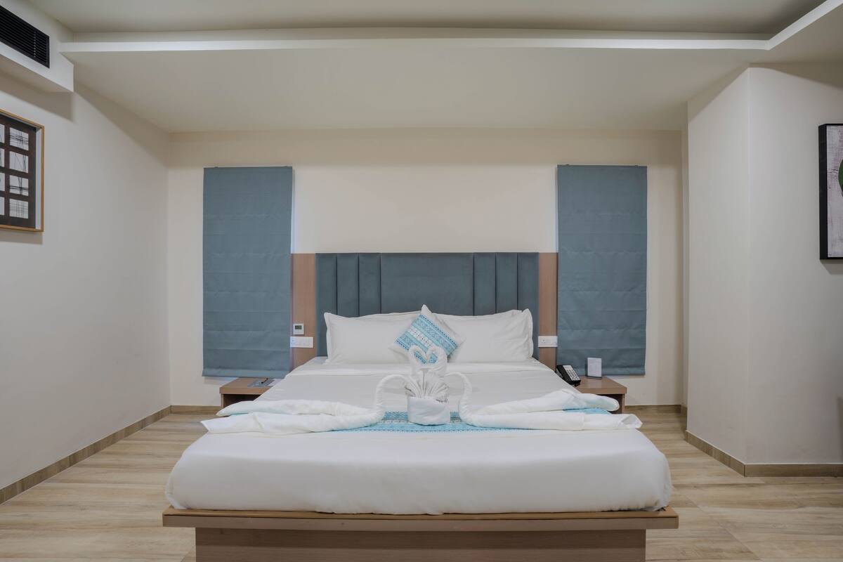 A modern hotel room with a large bed, a headboard, a nightstand, and a framed picture on the wall.