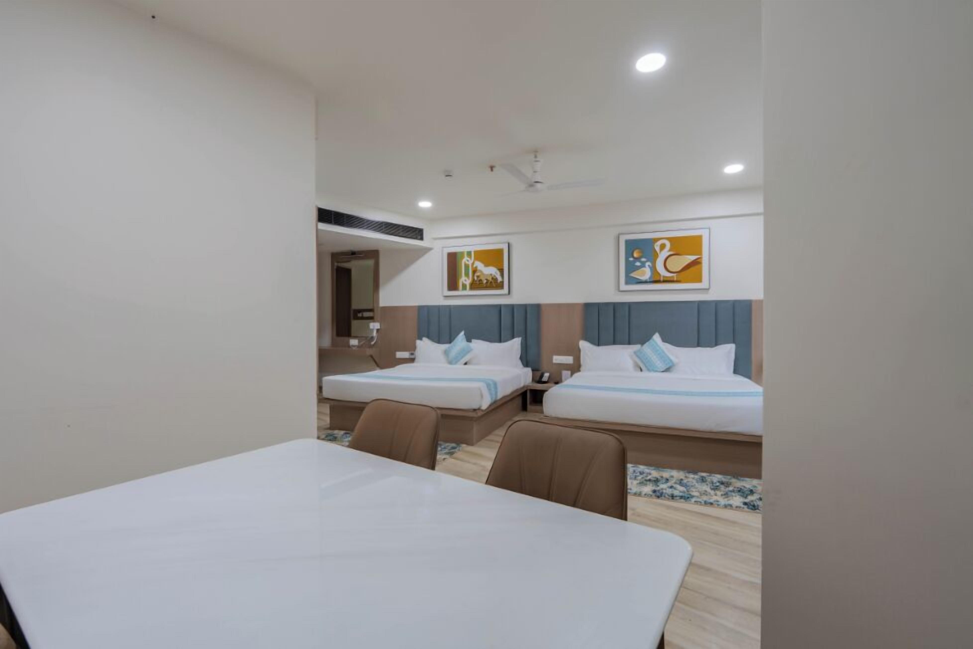 Quarto de hotel com duas camas de solteiro, uma mesa de jantar e uma kitchenette pequena.