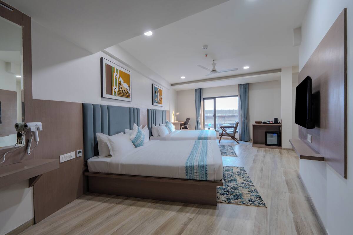 A hotel room with two beds, a flat-screen TV, a ceiling fan, and a large window with curtains.