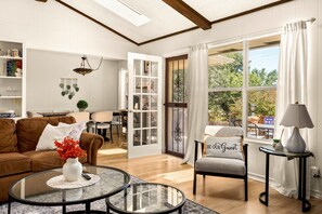 A well-lit living room with a glass coffee table, a brown sofa, and a chair with a 'BE OUR GUEST' pillow. - 5BR San Antonio Home - Large Private Pool, Covered Patio, BBQ & Outdoor Games (San Antonio)